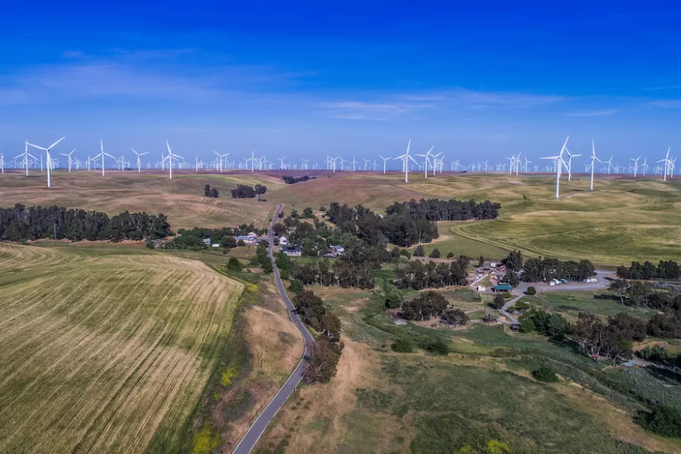 Aerial view of small community among green agricultural fields and wind turbines in Solano County, Northern California.